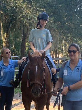 relationships and LEMS | Lambert-Eaton News | Grace rides a horse as two staff members walk on either side.