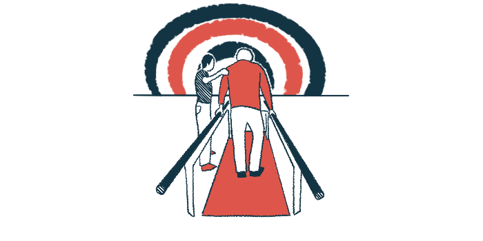 An older man is seen from behind walking between two parallel bars in therapy, as a therapist holds his left arm.